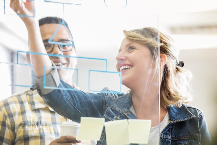 Business colleagues write ideas on transparent dry erase board