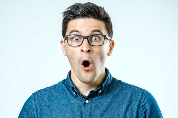 Portrait of young surprised man with opened mouth. Isolated on gray