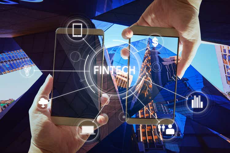 "Fintech" word on digital virtual screen with two businessman hands holding smartphones background.