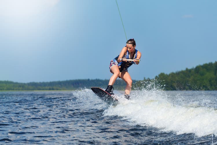 woman riding wakeboard on motorboat wave in lake