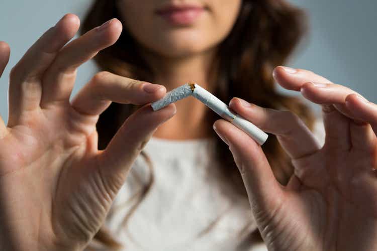 Woman breaking cigarette against white background