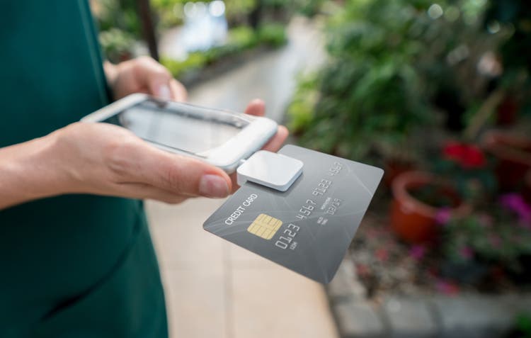 Close up of unrecognizable saleswoman doing the checkout using a credit card reader and smartphone