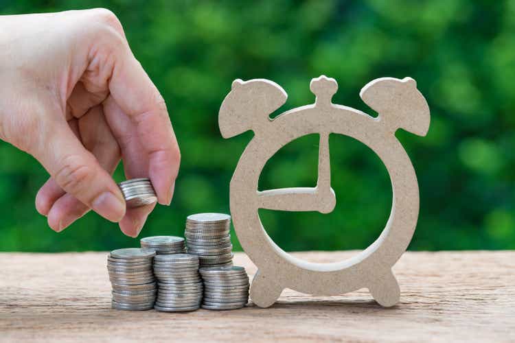 Woman hand holding stack of coins money putting on stack of coins and wooden alarm clock as long term investment timeline or savings concept