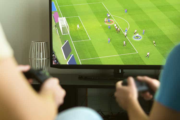 Two guys playing imaginary multiplayer soccer or football video game with console and tv.