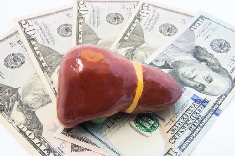 Liver figure lying on money - dollars banknotes. Photo for determining cost of treatment of liver diseases such as hepatitis C, cirrhosis, operations on liver and gallbladder, liver transplantation