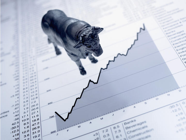 Bull figurine on ascending line graph and list of share prices