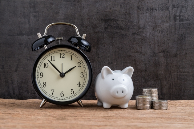 Retro alarm clock with white piggy bank and stack of coins on wooden table and black background as long term savining money or retirement investment concept