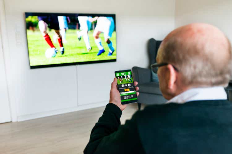 Man watches soccer match on television and bets on the game with betting app on phone
