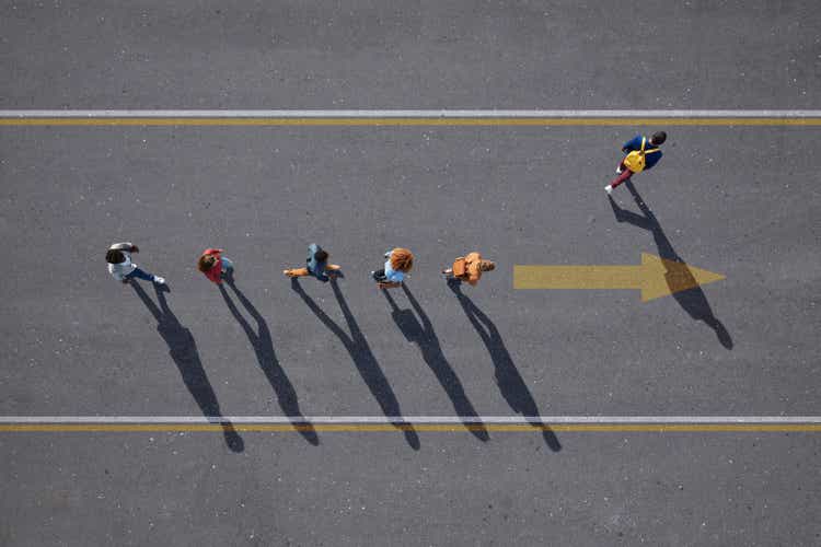 People walking in line on road, painted on asphalt, one person walking off.