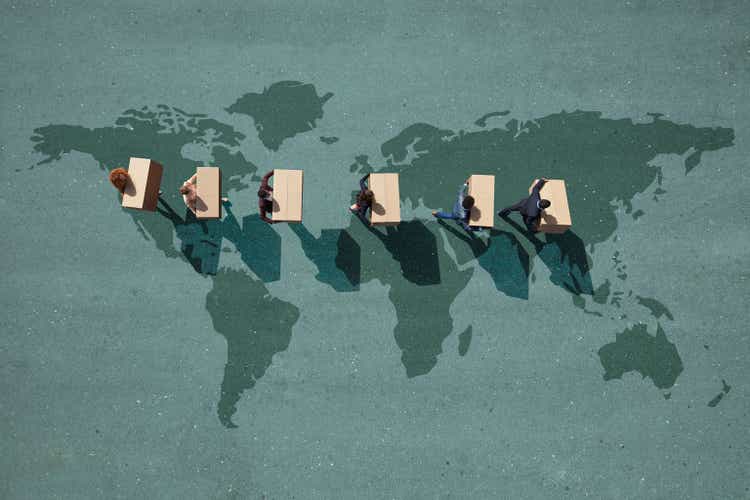 Businesspeople walking across painted world map, carrying moving boxes