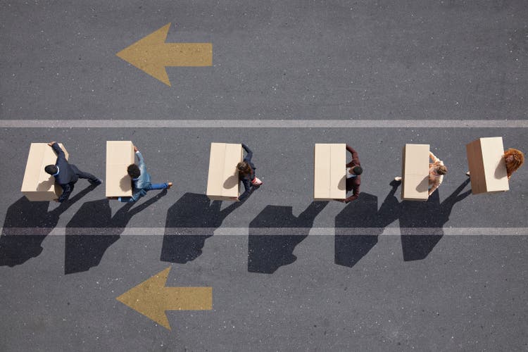 Businesspeople walking in lane with painted arrows, carrying moving boxes