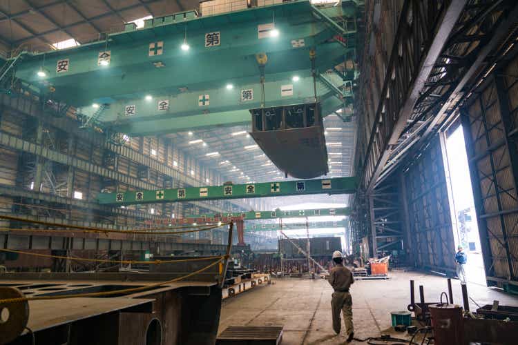 A worker walking through a large shipbuilding factory