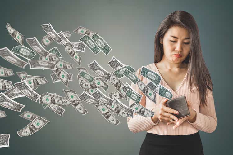 poor Asian woman holding purse having problem with money flying away, over spending concept