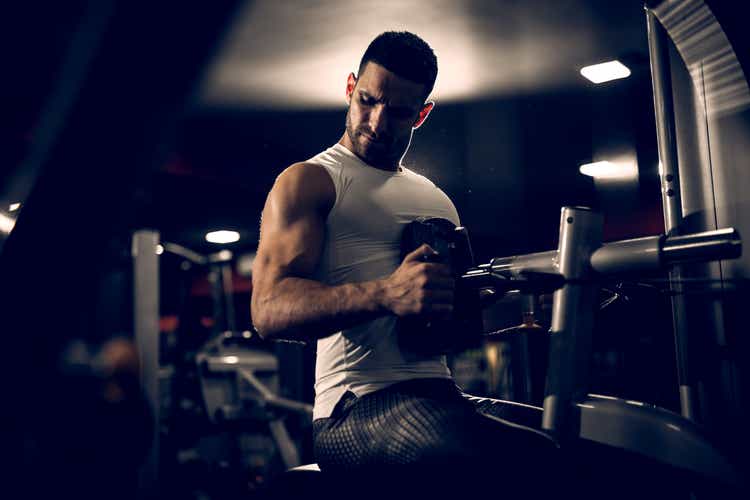 Close up of motivated focused strong muscular bearded man doing back and triceps exercise on the machine in the gym.