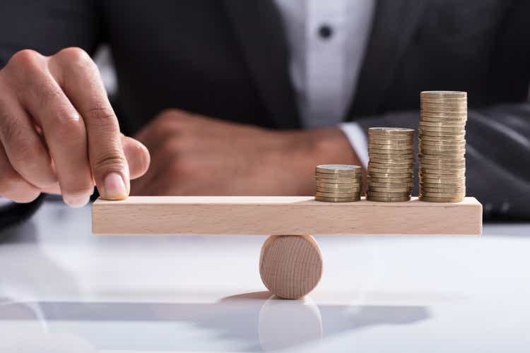 Businessperson Balancing Stacked Coins On Wooden Seesaw