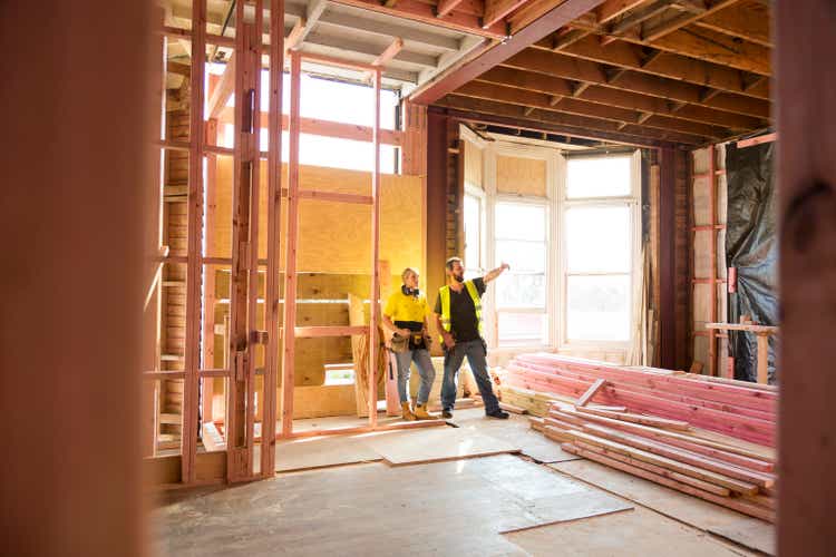 Two construction workers talk together inside large house under renovation