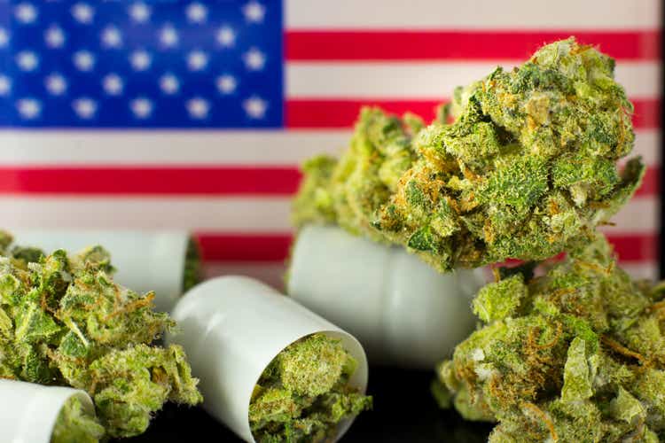 Medical Pills and tablets of Cannabis - marijuana flowers in white capsules with USA flag on the black mirror background.