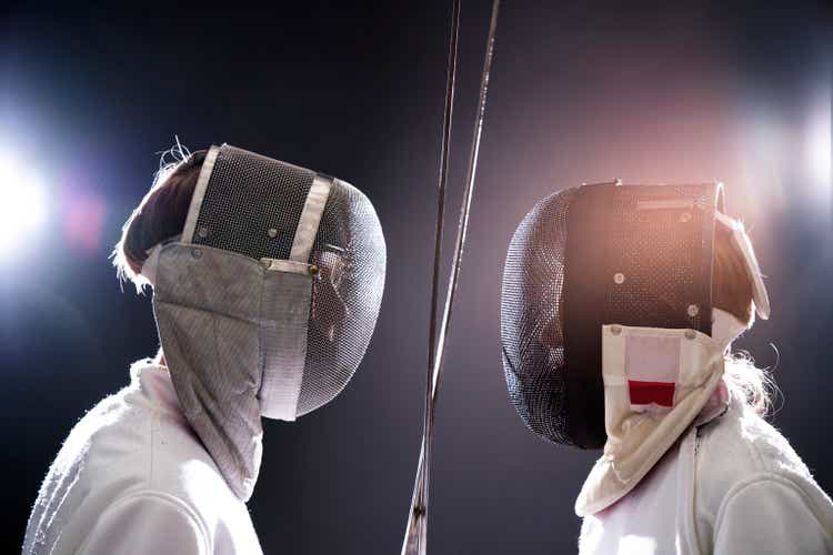 Boys with foils fencing against black background