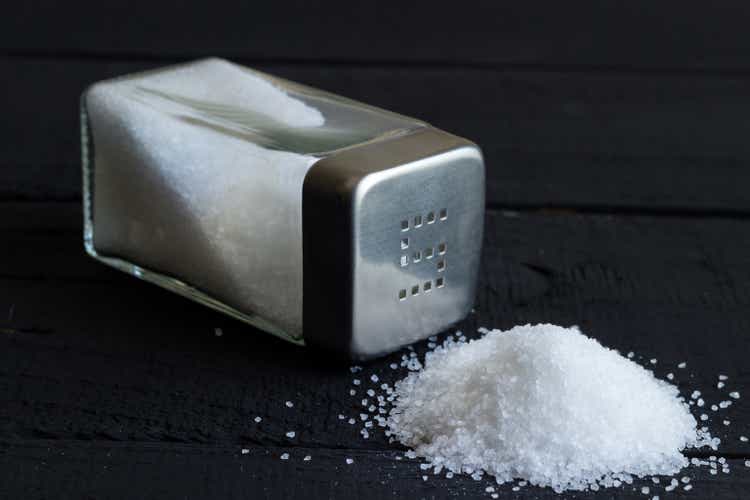 Glass salt shaker on black rustic table and heap of salt crystals with space for text in background