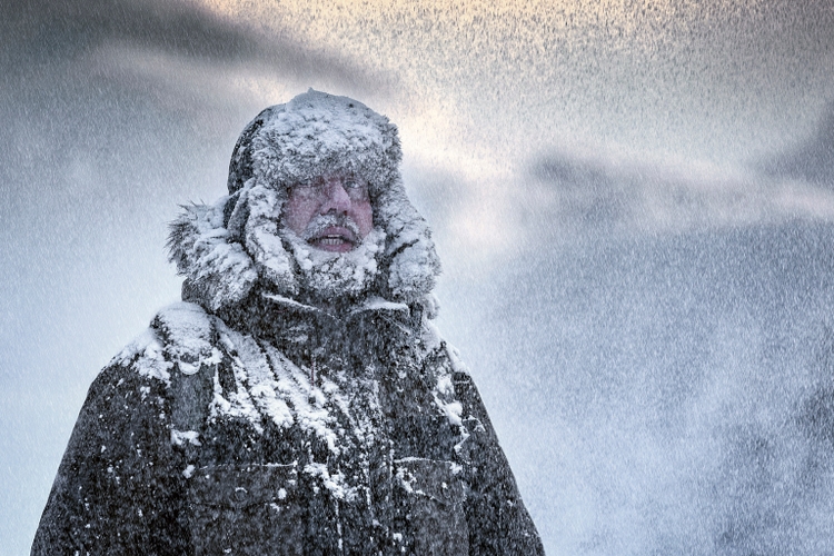 Wintery scene of a man with Furry and full beard shivering in a snow storm