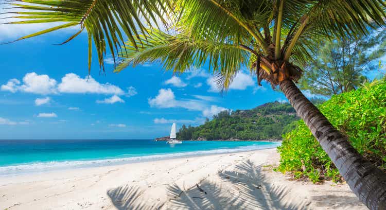 Sandy beach with palm trees and a sailing boat