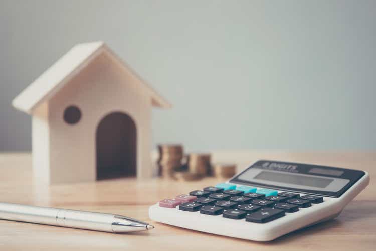 Calculator with wooden house and coins stack and pen on wood table. Property investment and house mortgage financial concept