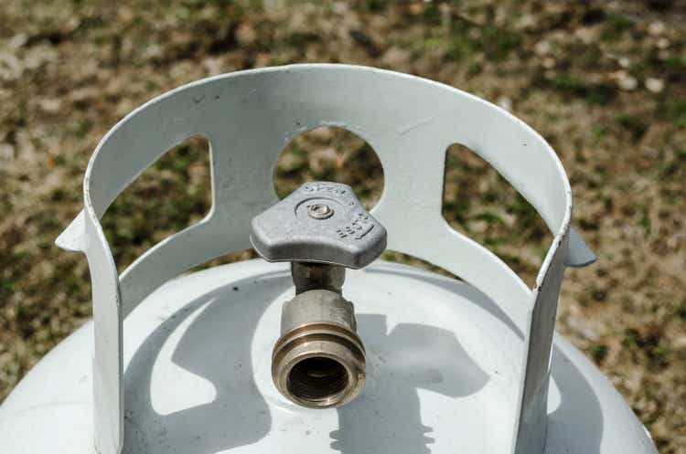 Angled overhead close-up of the top of a white propane tank and brass valve with grass in the background