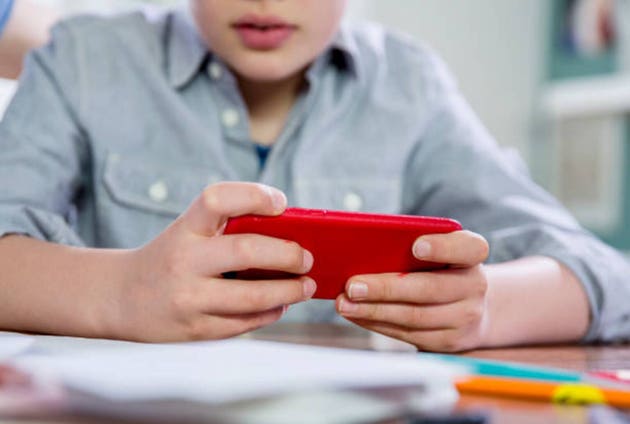 10 years old blonde school boy gaming with smart phone.