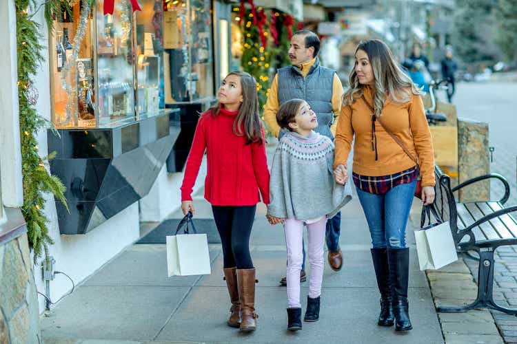 Family walking through mountain town with shopping bags, browsing stores.