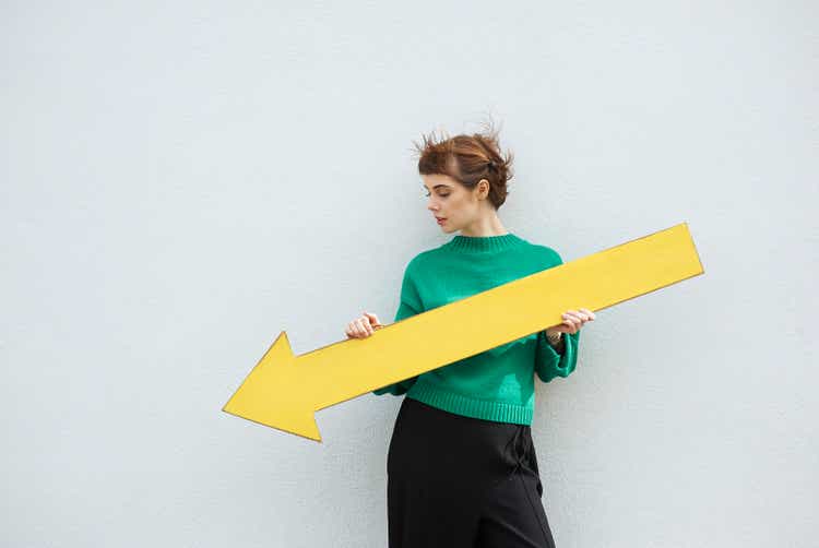 Young woman holding large yellow arrow sign pointing down.