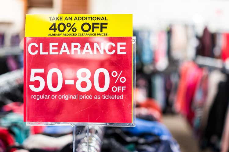 Many clothes bokeh in discount store, garments hanging on racks hangers row closeup with large red clearance sign, reduced prices