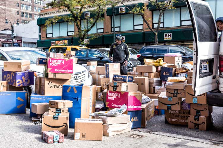 Delivery man with many boxes in NYC by BH photo video store, van truck unloading amazon prime, walmart, chewy, blue apron