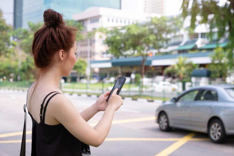 Young beautiful woman using phone to grab taxi in Singapore. Standing beside the road