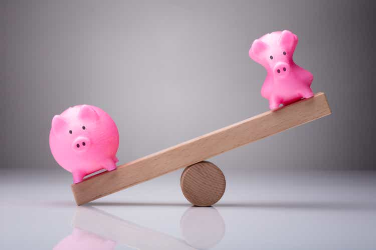 Unbalance Of Two Piggybanks On Wooden Seesaw