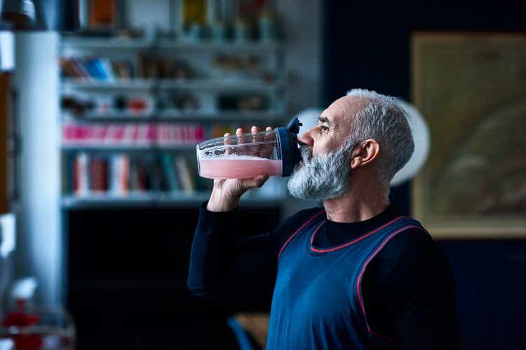 Senior man in sports top swallows healthy drink from container