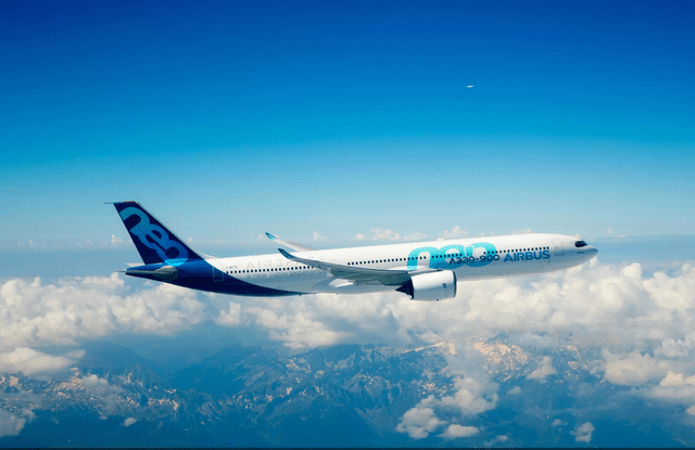 This image shows an Airbus A330neo wide body airplane in flight with clouds and mountains in the background.