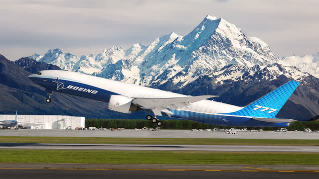 This image shows a Boeing 777F taking off with mountains in the background.